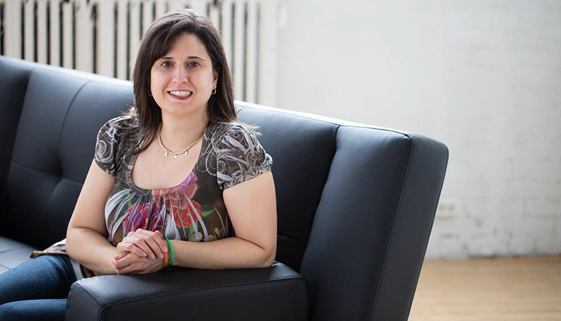 PIcture of a woman on a couch, leaning over the side, smiling at the camera.